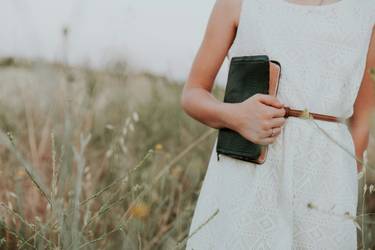 Junges Mädchen in einem weißen Kleid mit einem Buch in der Hand auf einer Wiese