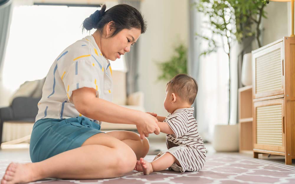 Mama hält ihr Baby an den Händen und hilft ihm zu sitzen