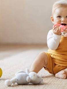 Baby sitzt auf dem Teppich und spielt mit einem rosa Beißring