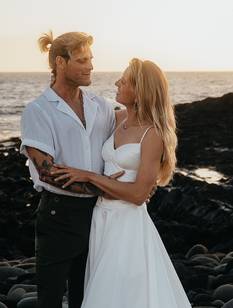 Hochzeitspaar am Strand in sommerlichem Hochzeitsoutfit lächelt sich verliebt an