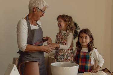 Oma mit ihren zwei Enkelinnen an einem Tisch mit Backzutaten