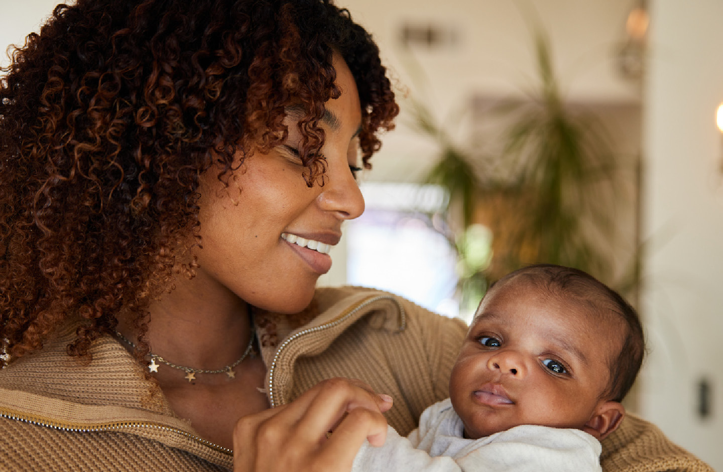 Lächelnde Mutter schaut ihr neugeborenes Baby an, das sie im Arm hält