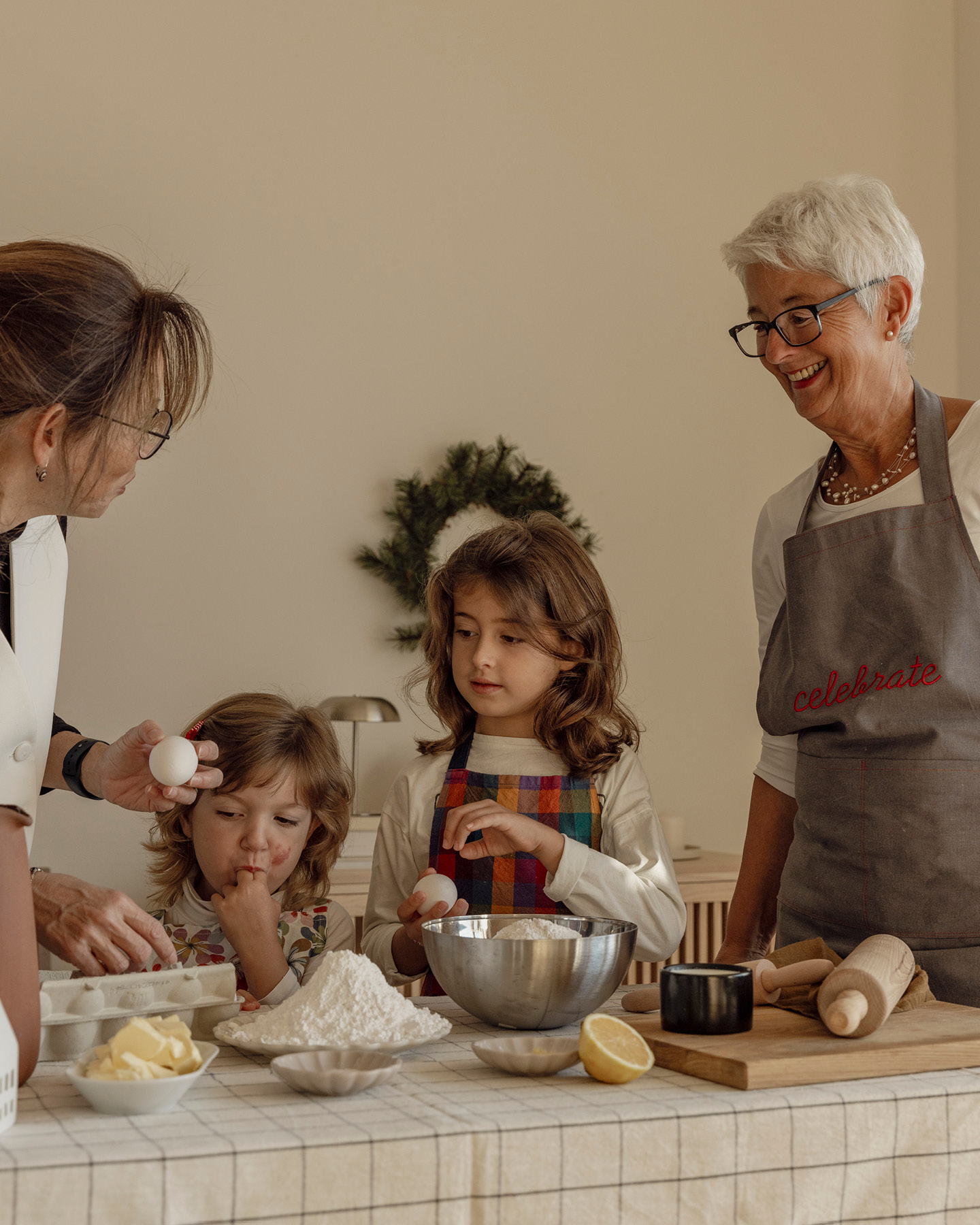 Oma mit zwei kleine Mädchen und deren Mutter an einem Tisch mit Backzutaten